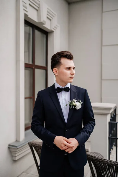 Young man in a black jacket with a bud of flowers stands on street near building — Stock Photo, Image