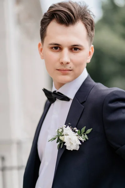 Jeune homme vêtu d'une veste noire avec un bourgeon de fleurs se tient sur la rue près du bâtiment — Photo