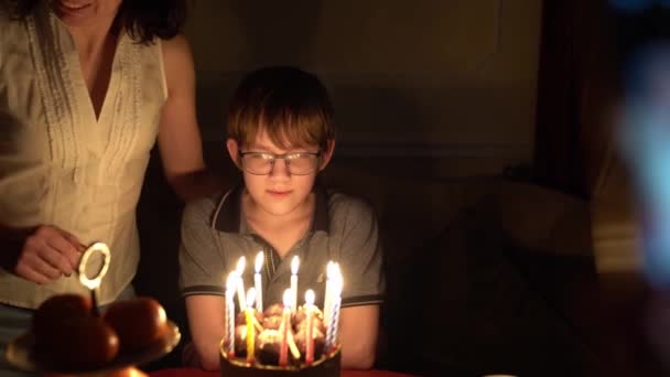 Стрельба в темноте. Мальчик в очках задувает свечи на торте.. — стоковое видео