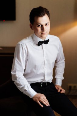 Beyaz gömlekli ve papyonlu genç adam sandalyede oturuyor. iş portresi