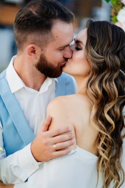 Yeni evliler öpüşür. Uzun bukleli, beyaz, zarif elbiseli gelin.