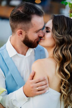 Yeni evliler öpüşür. Uzun bukleli, beyaz, zarif elbiseli gelin.