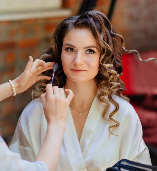The make-up artist does makeup to the bride in the yard of the house