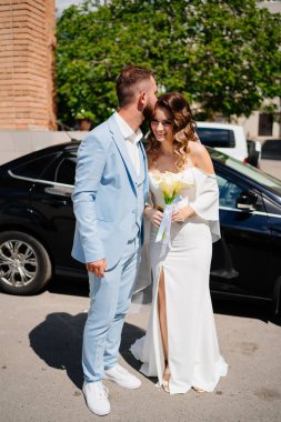 Mavi takım elbiseli damat ve siyah arabalı zarif beyaz elbiseli gelin.