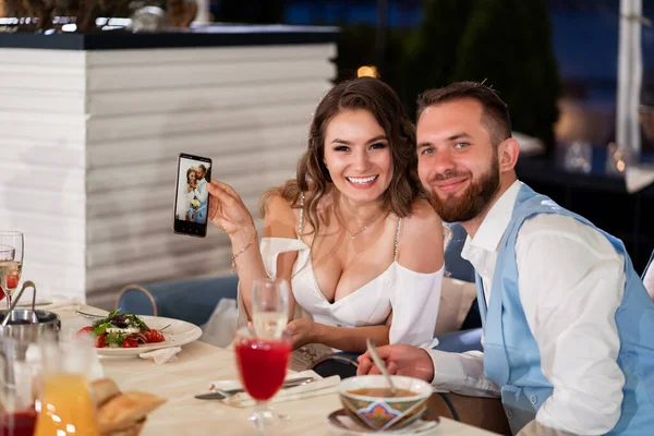 Невеста и жених смотрят на фото на телефоне, сидящем за столом на банкете. — стоковое фото