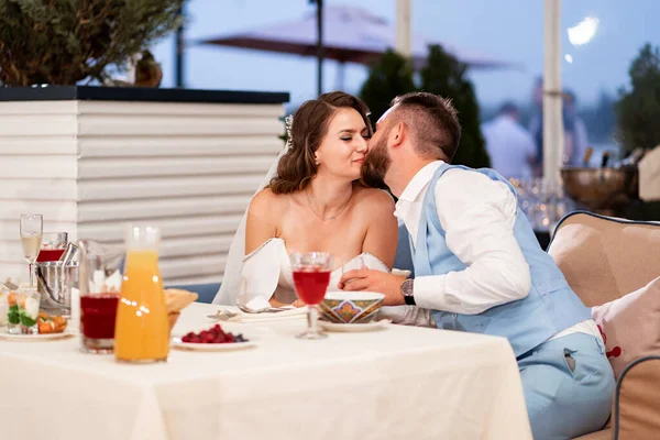 Молодожены целуются и обнимаются в ресторане и слушают поздравления от гостей. — стоковое фото