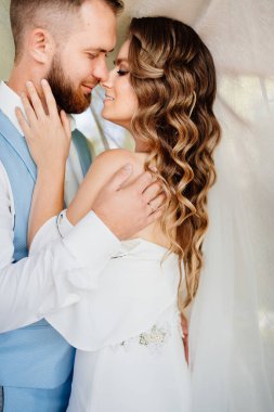 Yeni evliler parkta beyaz bir perdenin yanında dikiliyorlar..