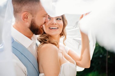 Peçenin altında Mutlu ve güzel gelin ve damat parkta nazikçe sarılıyorlar