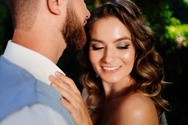 Mutlu ve güzel gelin ve damat parkta nazikçe sarılıyor.