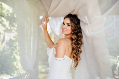 Güzel gelin parktaki beyaz bir perdenin yanında duruyor..