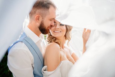 Peçenin altında Mutlu ve güzel gelin ve damat parkta nazikçe sarılıyorlar