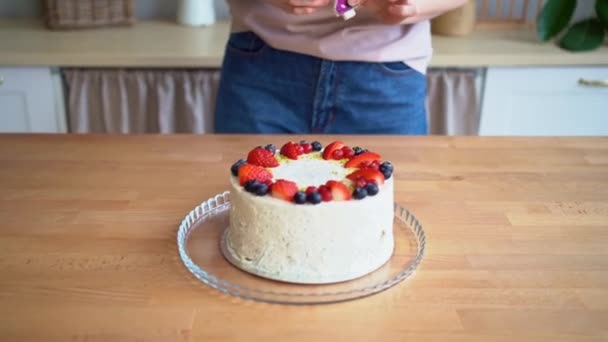 En kvinna i köket sätter ett ljus i form av siffran 2 på tårtan — Stockvideo