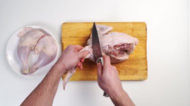 Erkek elleri çiğ tavuk leşini tahta bir kesme tahtasının üzerinde doğruyor.
