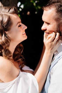 Kapat. Mutlu ve güzel gelin ve damat parkta nazikçe sarılıyor. Bahçedeki bir düğün çekiminde aşık bir çift. nazik dokunuşlar. 