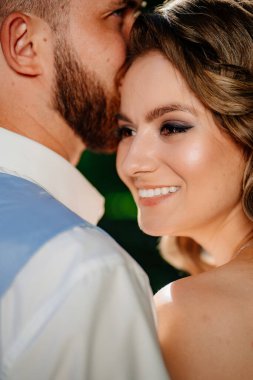 Mutlu ve güzel gelin ve damat parkta nazikçe sarılıyor. Bahçedeki fotoğraf çekiminde aşık bir çift..