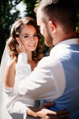 Kapat. Mutlu ve güzel gelin ve damat parkta nazikçe sarılıyor. Bahçedeki bir düğün çekiminde aşık bir çift. nazik dokunuşlar. 