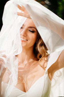 Duvağının altında uzun bukleleri olan güzel bir gelin. narin bir kadın portresi. Düğün makyajı. Doğal güzellik..