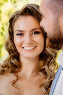 Mutlu ve güzel gelin ve damat parkta nazikçe sarılıyor. Bahçedeki fotoğraf çekiminde aşık bir çift..