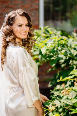 Beyaz ipek bornozlu gelin evinin bahçesinde duruyor.