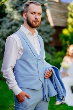 Genç bir adam, mavi takım elbiseli damat ve yaz bahçesinde sakallı.