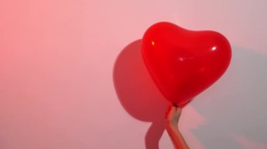 Renkli bir ışıkta beyaz bir duvara karşı elinde bir kalp şeklinde kırmızı balon. 