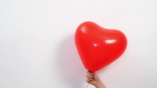 Um balão vermelho em forma de coração na mão contra uma parede branca. — Vídeo de Stock