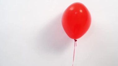 Beyaz bir duvara karşı ip üzerinde kalp şeklinde kırmızı bir balon.. 