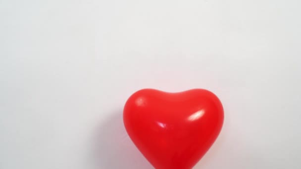 Un ballon rouge en forme de coeur sur une corde contre un mur blanc s'envole. — Video