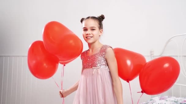 Adolescente chica danzas, risas con rojo bolas de corazones en la cama cerca de blanco pared — Vídeo de stock