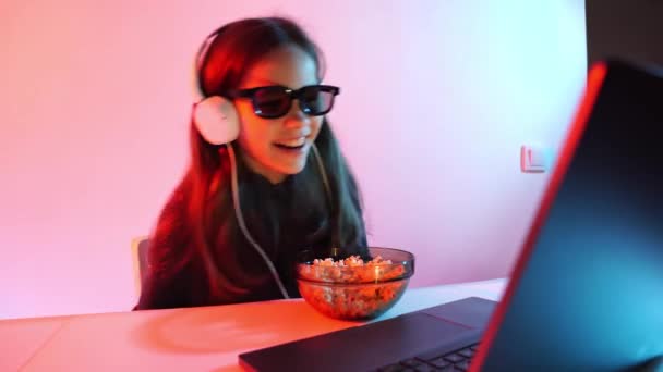 Chica en gafas 3D y auriculares relojes película divertida en el ordenador portátil, come palomitas de maíz — Vídeos de Stock
