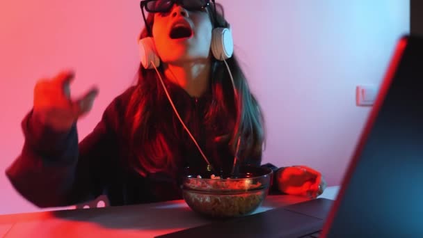 Девушка в очках для 3D и наушников смотрит фильм на ноутбуке, бросает попкорн — стоковое видео