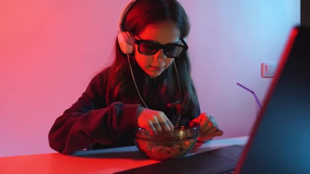 Menina em óculos para 3D e fones de ouvido assiste filme no laptop, lança pipoca — Vídeo de Stock