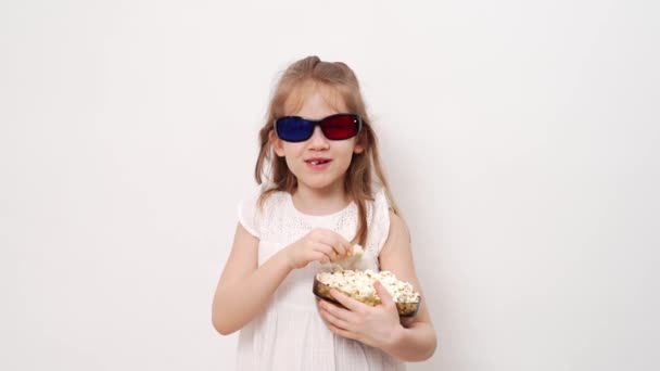 Flicka med glasögon för att titta på 3D-filmer med popcorn står mot vit vägg. — Stockvideo