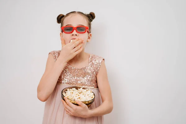 Adolescente chica con gafas para ver películas en 3D come palomitas de maíz contra la pared blanca. —  Fotos de Stock