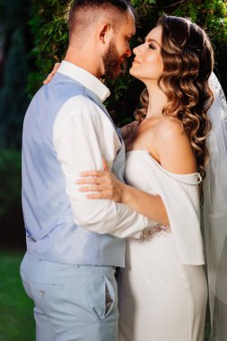 Mutlu ve güzel gelin ve damat parkta nazikçe sarılıyor.