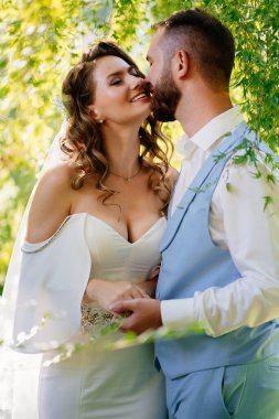 Mutlu ve güzel gelin ve damat parkta nazikçe sarılıyor.