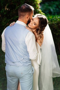 Mutlu ve güzel gelin ve damat parkta nazikçe sarılıyor.