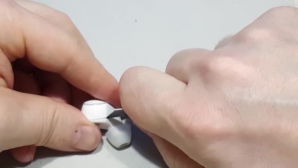 Mens hands disassemble a white wireless earpiece with a stationery knife. — Stock Video