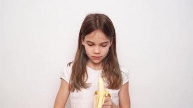 Tatlı bir genç kız, beyaz bir duvara karşı muz temizler ve yer..