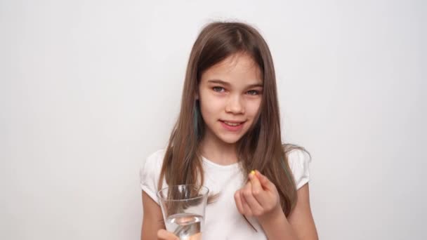 Een tienermeisje stopt een pil in haar mond en spoelt weg met water tegen een witte muur — Stockvideo