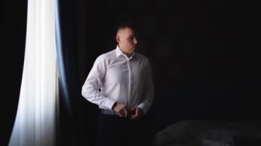 Pencere kenarında duran bir adam kemerini takar.. 