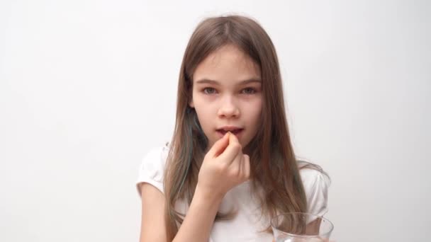 Seorang gadis remaja menaruh pil di mulutnya dan membasuh diri dengan air dinding putih — Stok Video