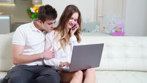 Un homme empêche une jeune belle femme de travailler sur un ordinateur portable et de parler au téléphone — Video