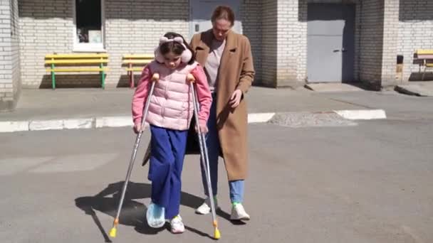 Moeder helpt haar dochter leren lopen op krukken. — Stockvideo