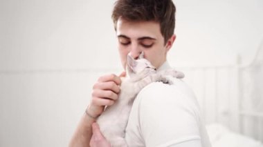 Genç bir adam küçük beyaz bir kedi yavrusu tutuyor ve onu okşuyor. nevsky maskeli kedi.