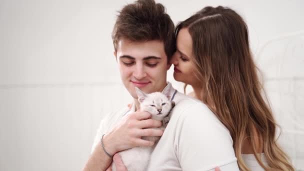 Una hermosa pareja de jóvenes amantes sosteniendo un pequeño gatito blanco. — Vídeo de stock