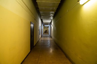 Dar, aydınlık, sarı duvarlı uzun koridor. 