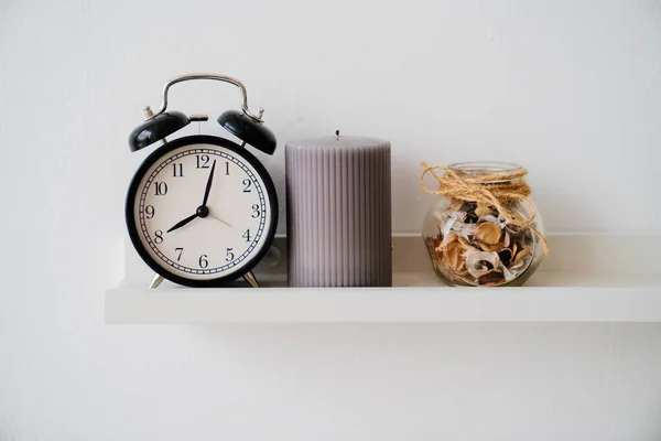 Reloj despertador negro, tarro con flores secas y perfume y vela gris en el estante. —  Fotos de Stock