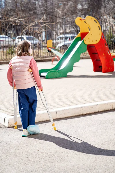Adolescente chica con una pierna rota en muletas en el patio de recreo. — Foto de Stock