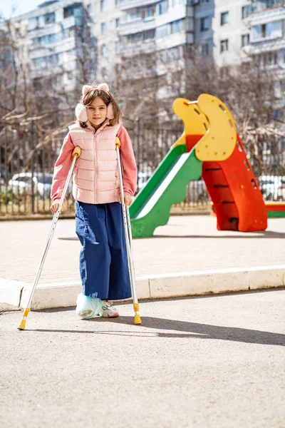 Adolescente chica con una pierna rota en muletas en el patio de recreo. — Foto de Stock